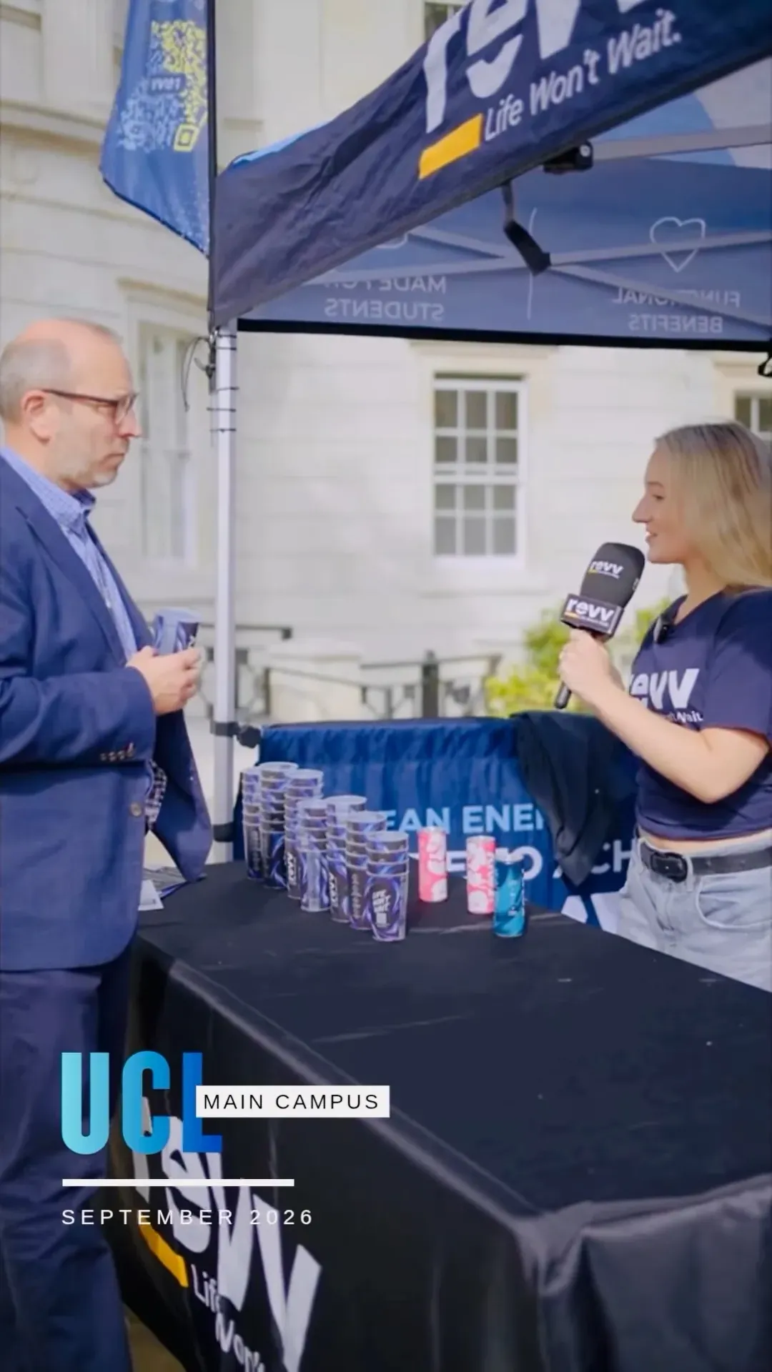 A UCL professor holding a can of revv at the stand, next to a table of revv cans.